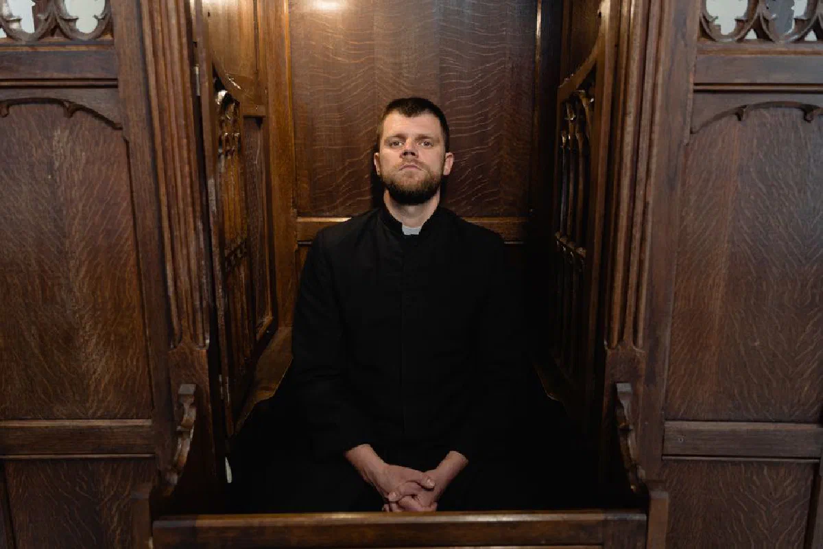 A solemn priest in a wooden confessional booth, embodying faith and tradition.