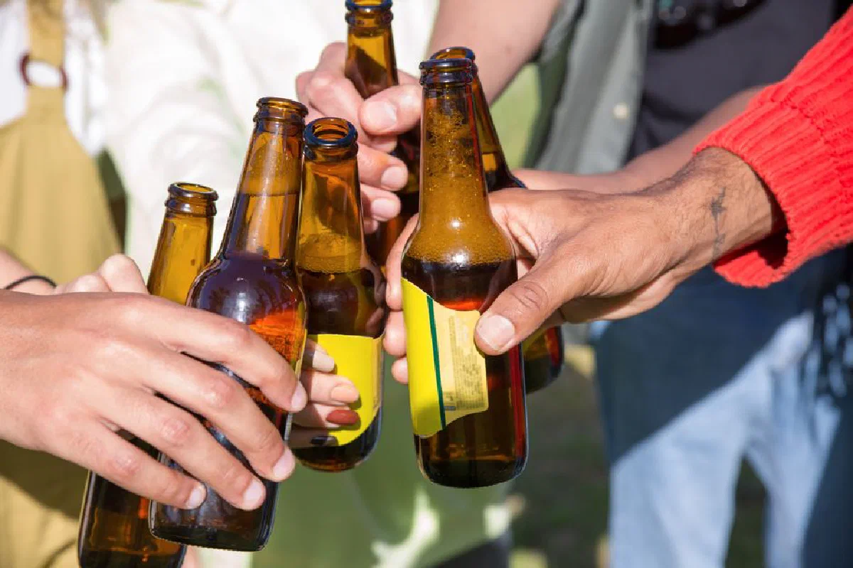 A group of people clinking beer bottles together in a celebratory toast outdoors.