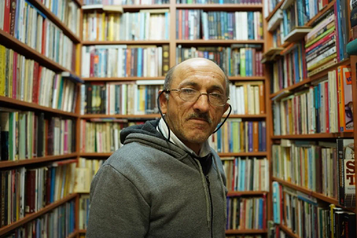 Portrait of an elderly man in a cozy Istanbul library wearing eyeglasses and a hoodie.