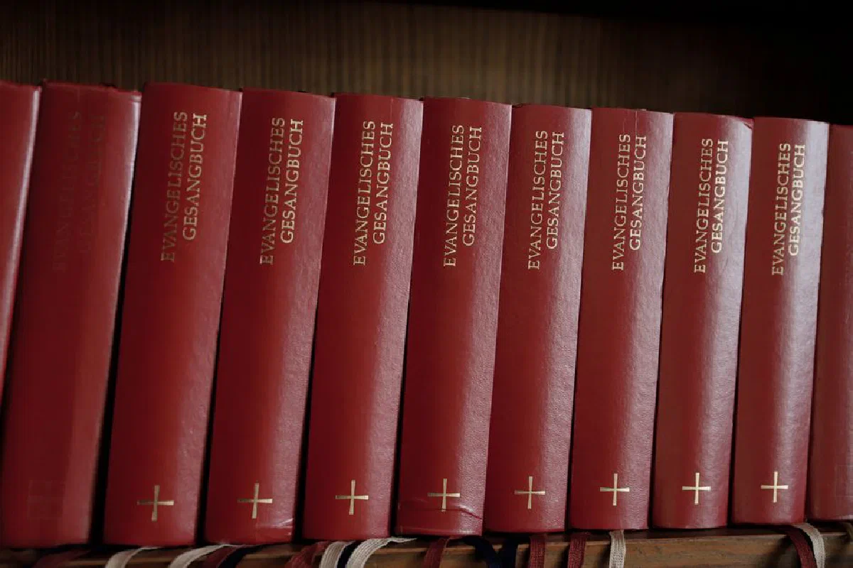 Row of red Evangelisches Gesangbuch hymnals on a wooden shelf, perfect for church and religious stock imagery.
