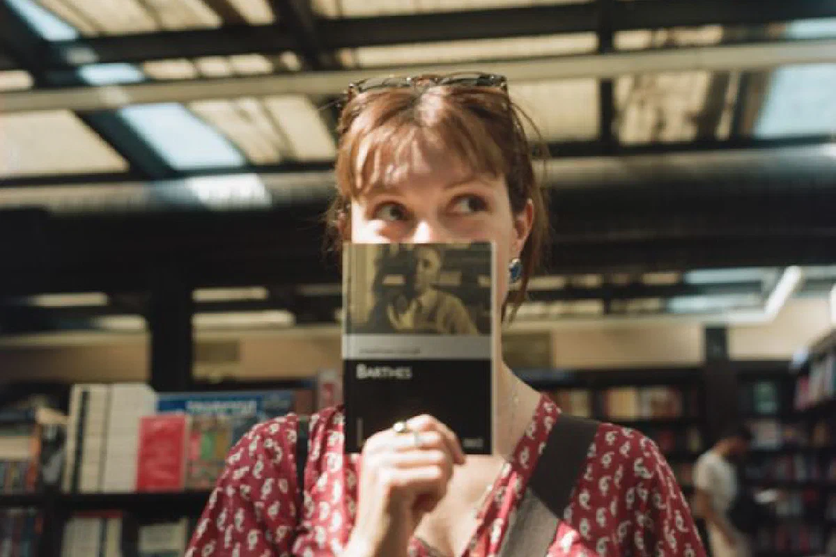 Woman holds a book in a sunlit Ankara bookstore, creating a playful and intellectual atmosphere.