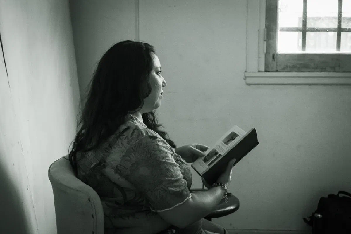Monochrome image of a woman reading a book by a window, captured indoors.