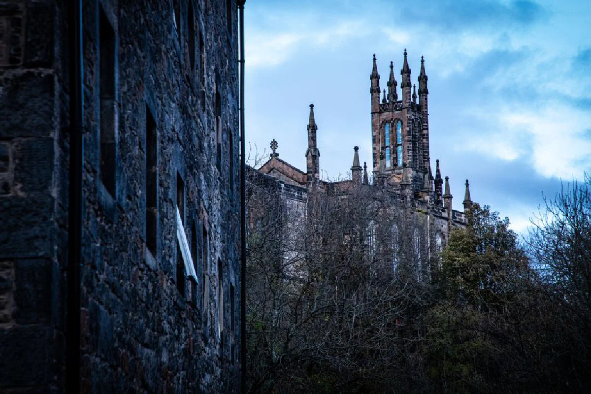 Gothic-style castle facade and tower against a cloudy sky, showcasing historical architecture.
