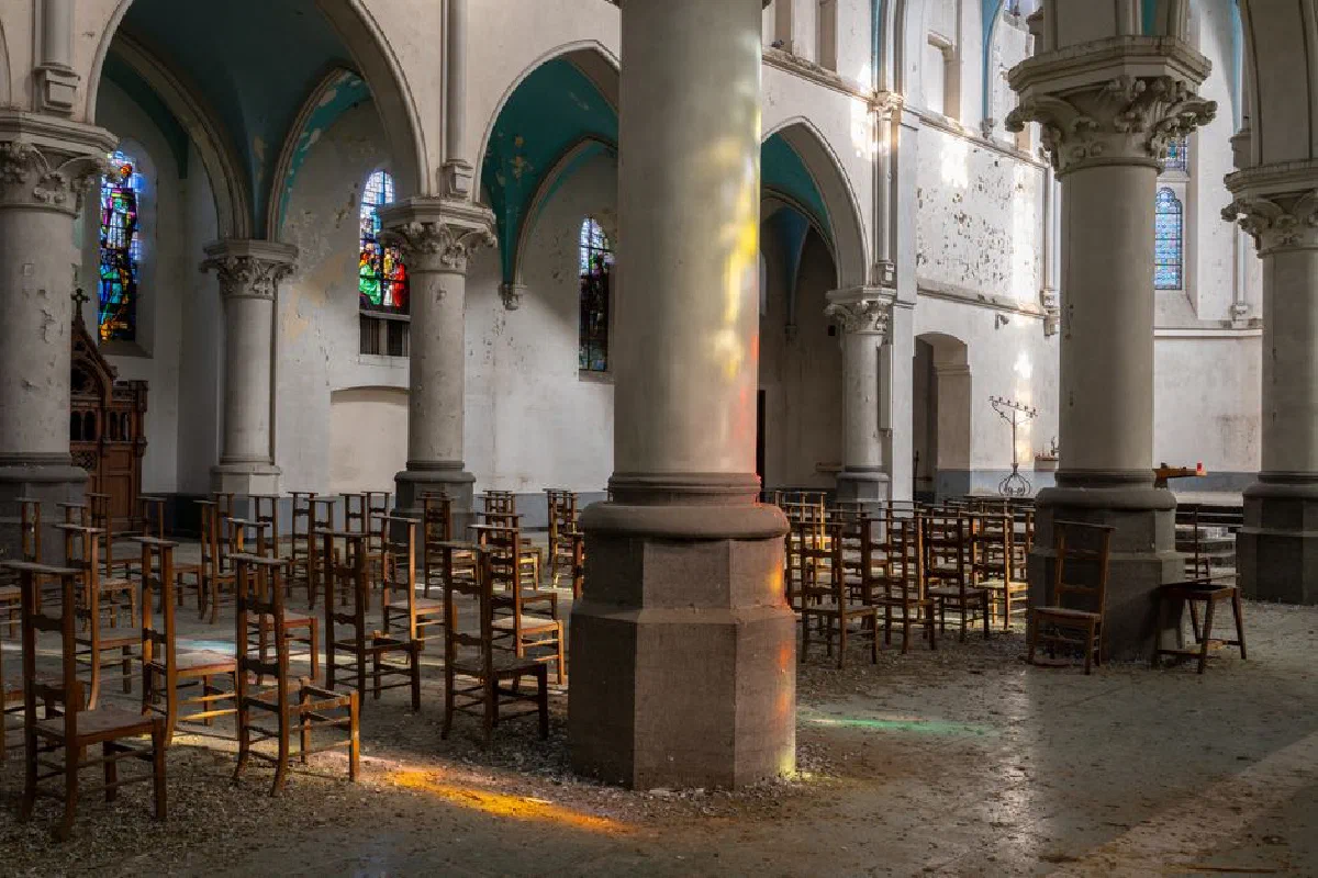 Sunlit stained glass reflections in an abandoned church interior with empty chairs.