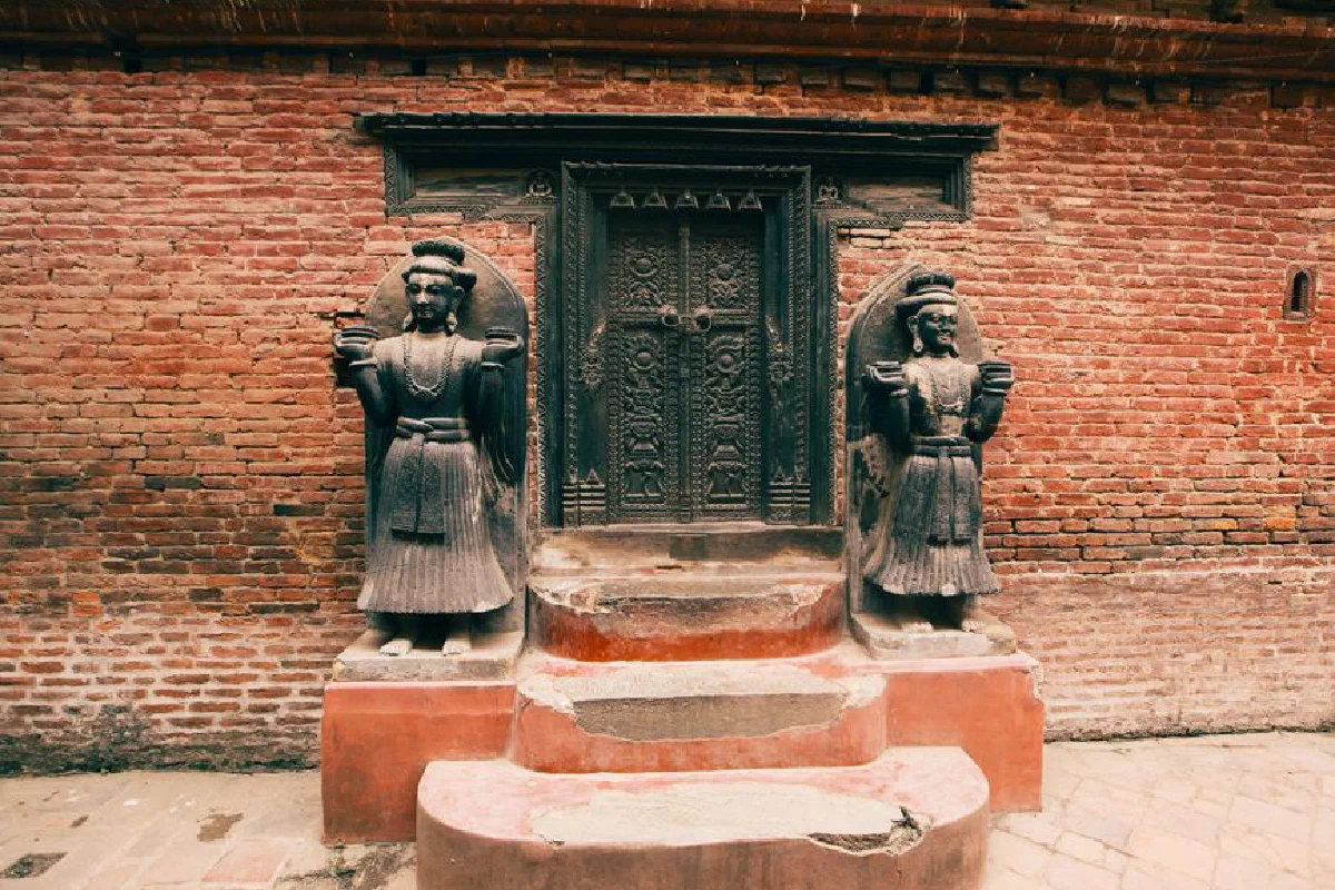 A detailed view of a temple entrance with ornate door and carved statues flanking brick walls.