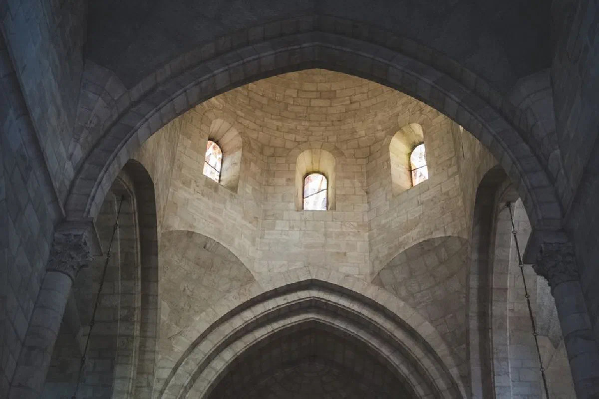 Intricate stone arches and stained glass windows inside a historic church in Jerusalem, showcasing Gothic architecture.