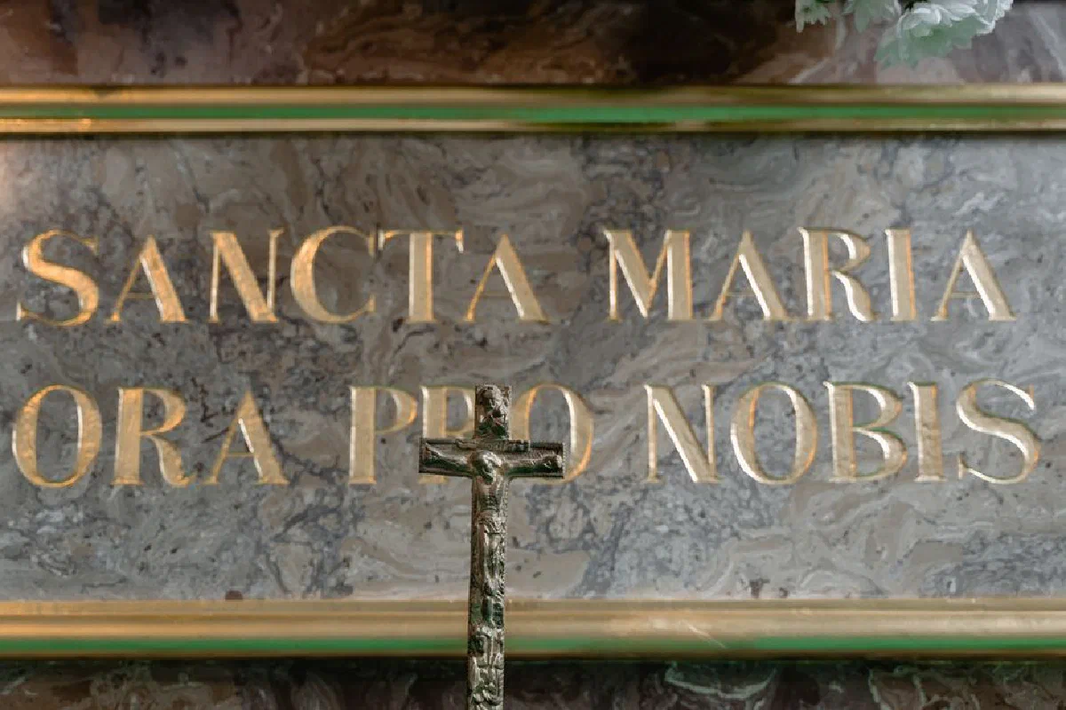 Detailed crucifix set before a sacred marble inscription 'Sancta Maria Ora Pro Nobis'.