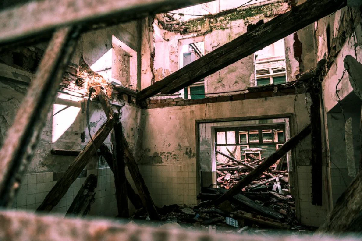 Crumbling interior of an abandoned building with collapsing beams and debris.