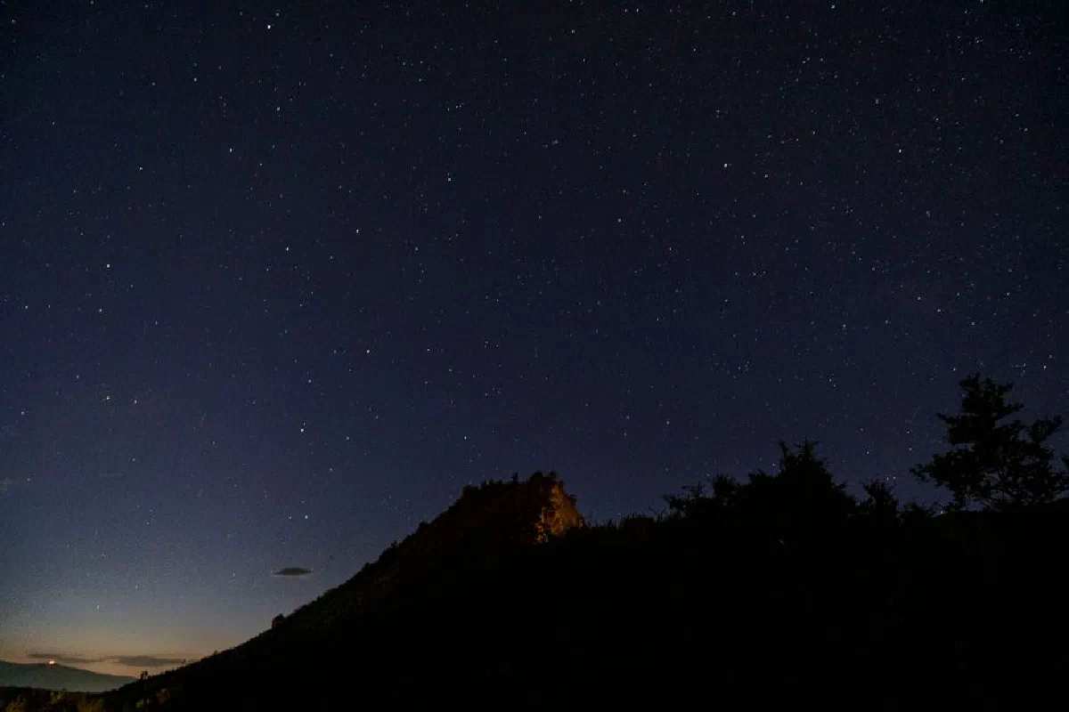 A stunning view of a starry night sky above a silhouette of a mountain, showcasing the beauty of nature.
