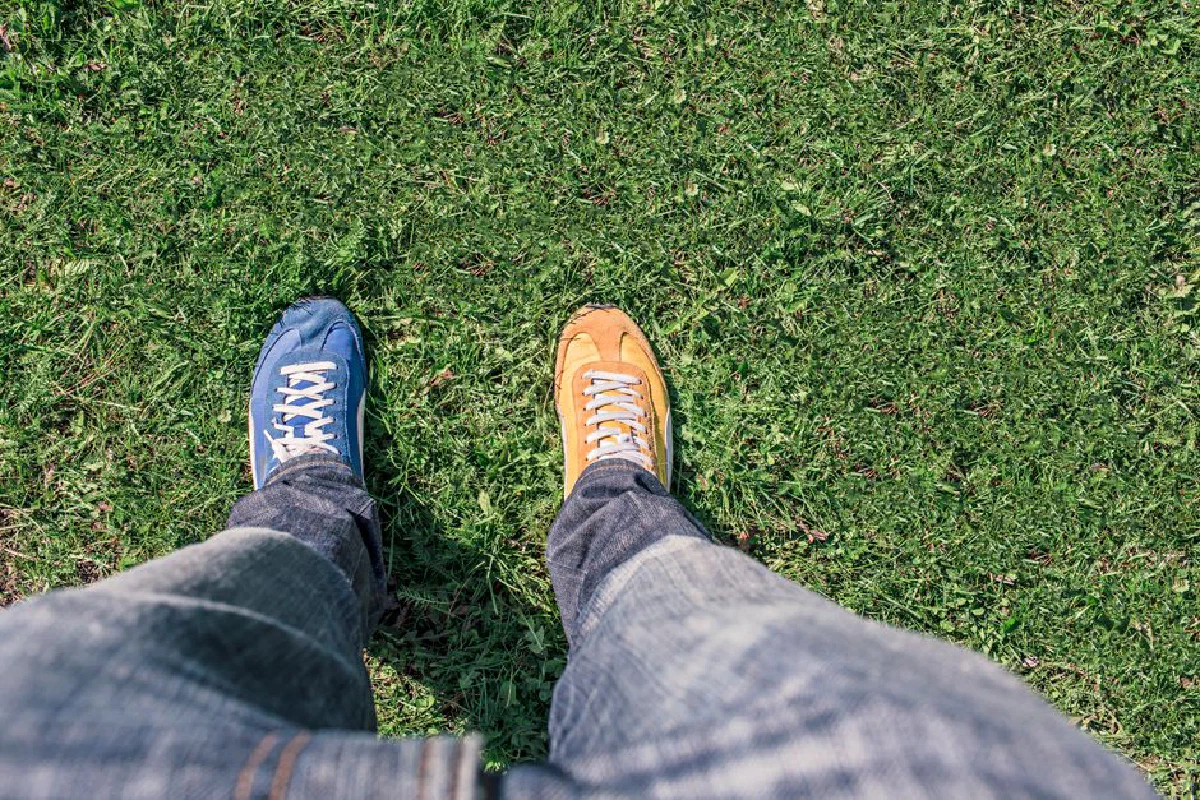 A person wearing mismatched shoes stands on green grass, highlighting differences and individuality.