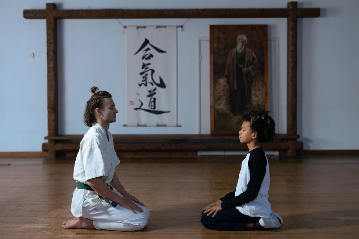 A karate trainer and child meditating on a wooden floor in a dojo setting.