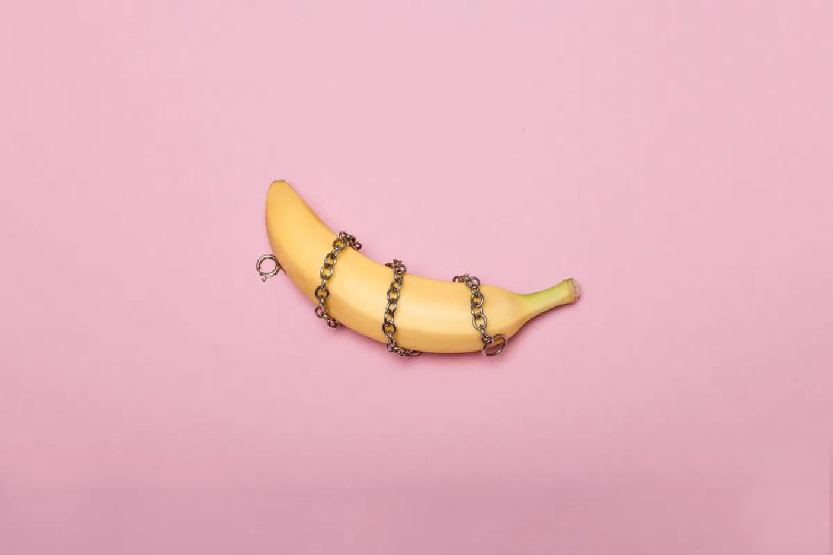 A banana wrapped in a metal chain on a pink background, representing conceptual art.