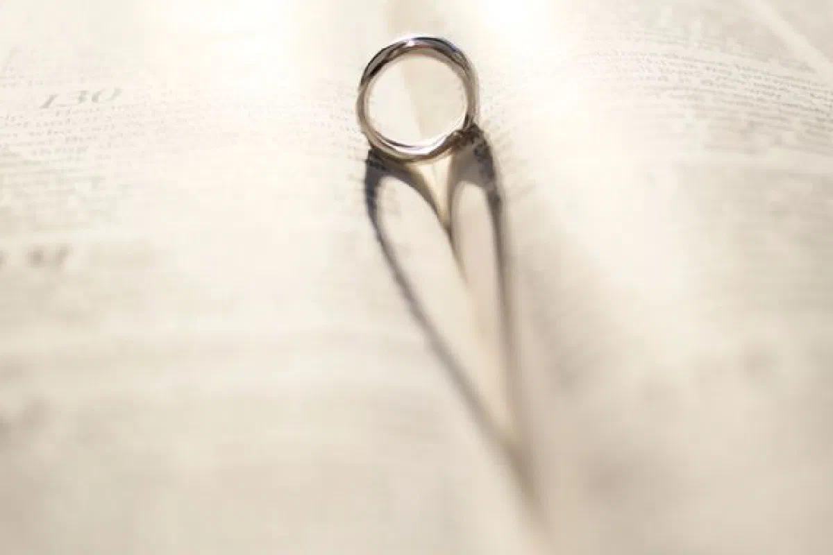 A silver wedding ring casting a heart-shaped shadow on an open book page.