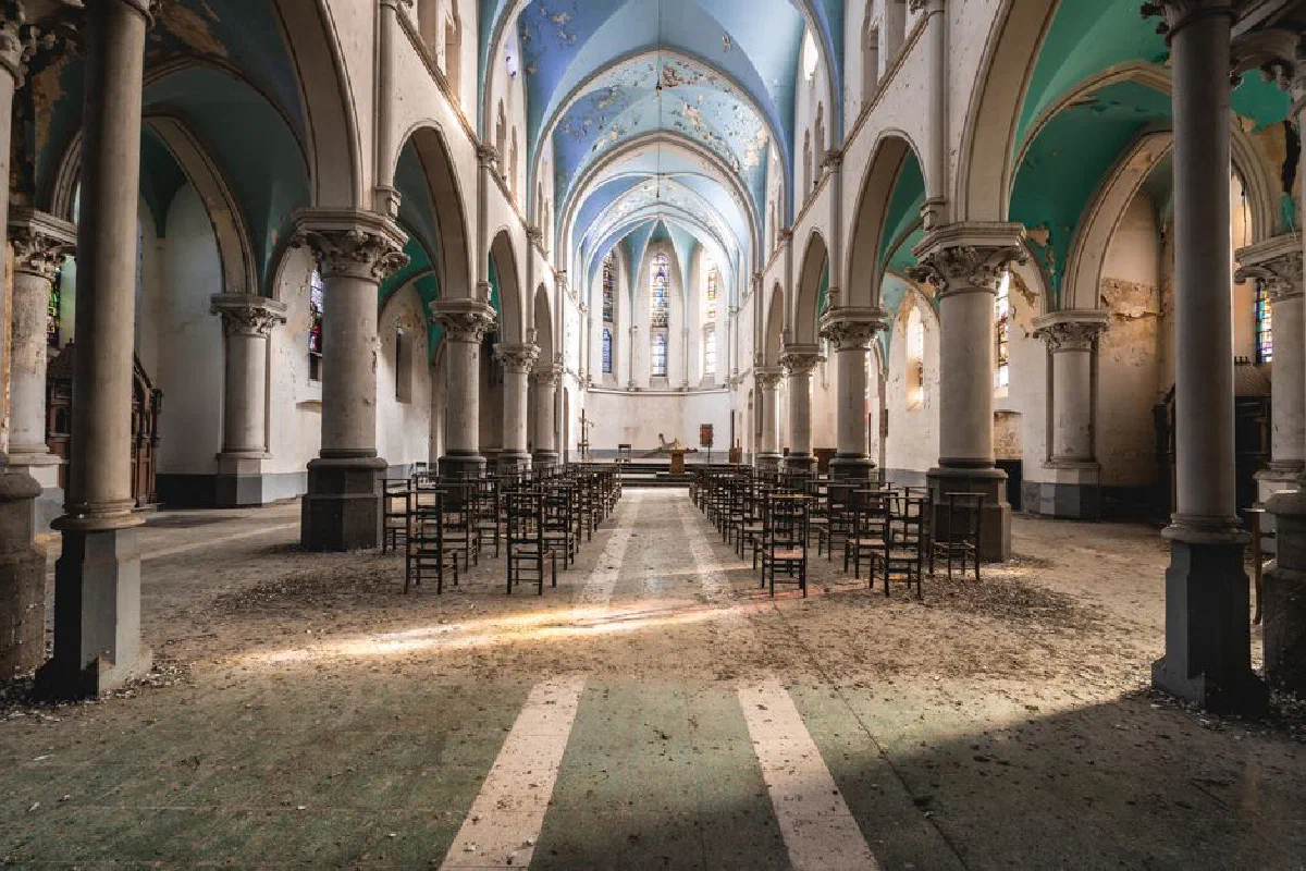 Wide-angle view of an abandoned gothic church interior featuring arched columns and scattered chairs.