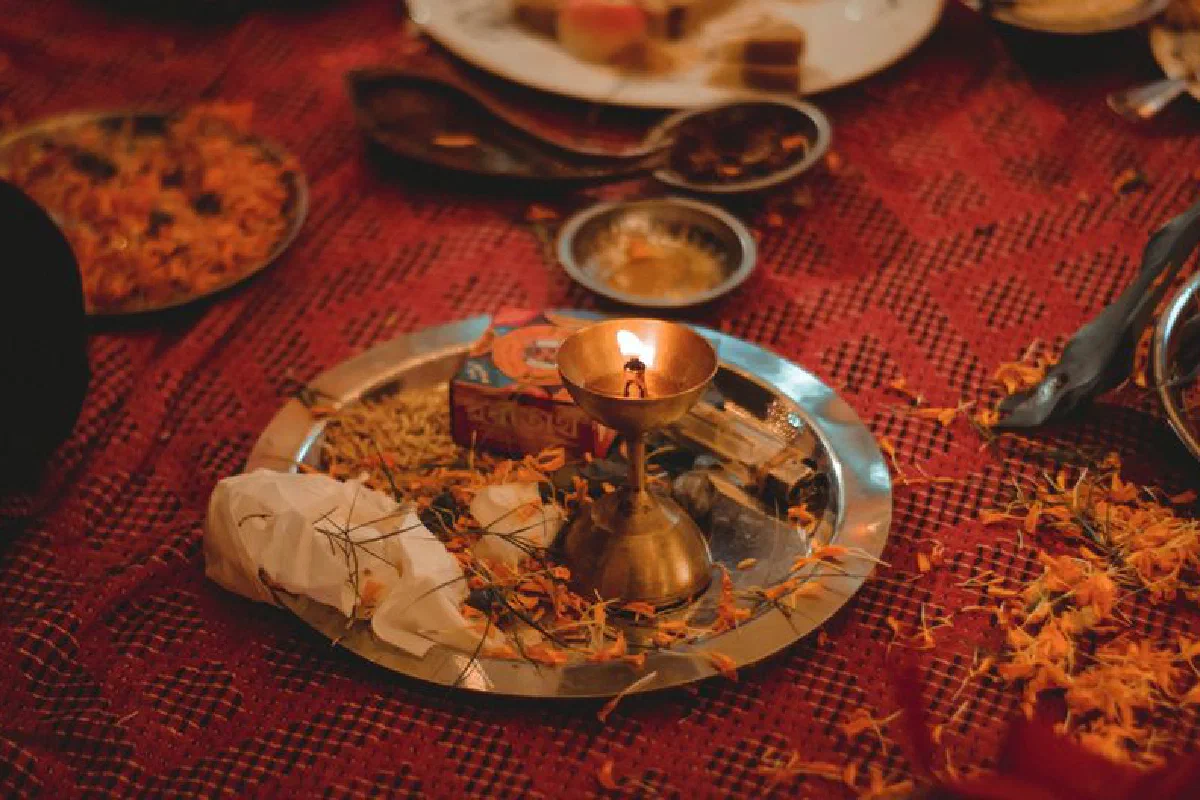 A traditional Indian ritual scene with an oil lamp and flower petals on a red cloth.