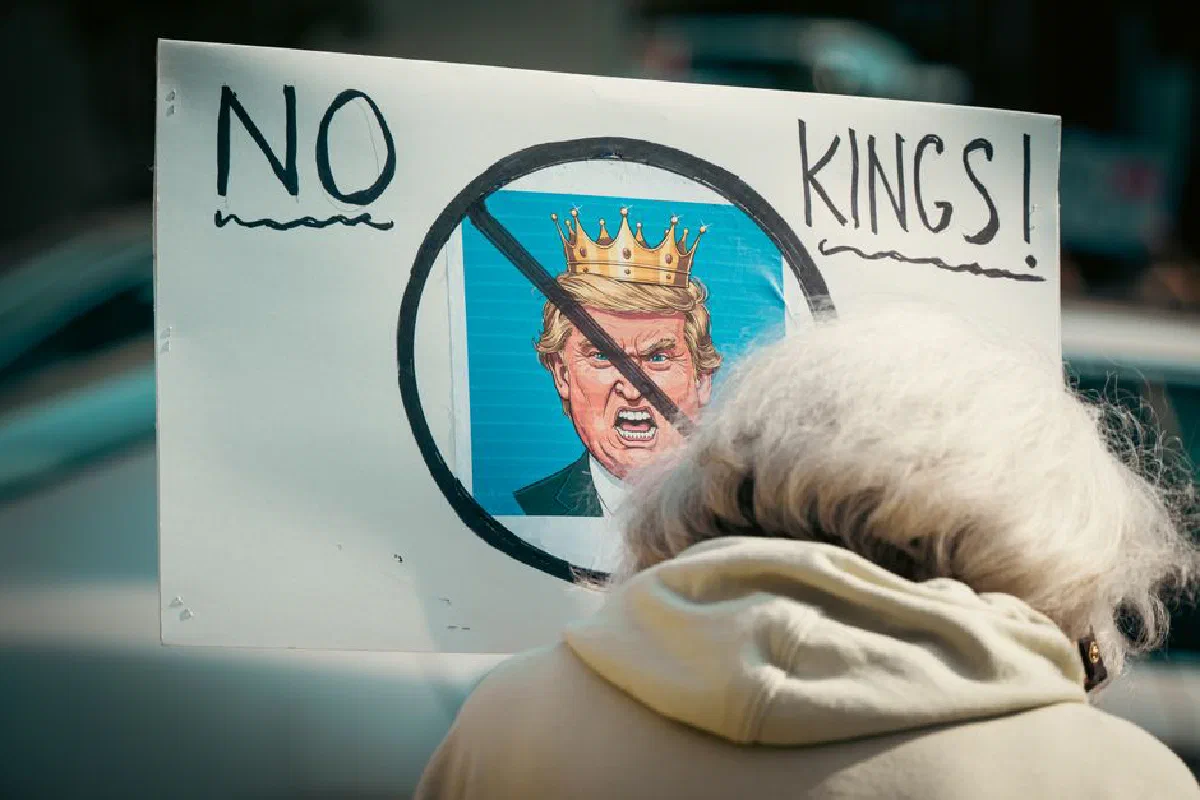 A protest sign reading 'No Kings' depicts resistance against monarchy with a satirical image.