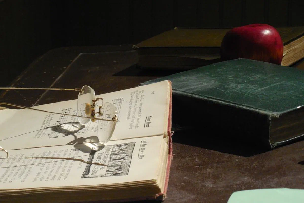 A collection of vintage books and eyeglasses on a wooden desk, creating a nostalgic ambiance.