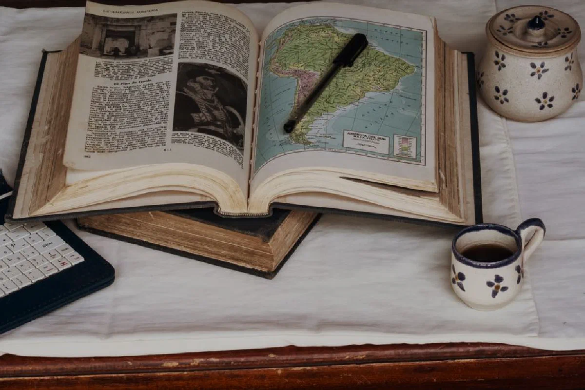 An open vintage book showing a map of South America, accompanied by a pen and a cup of coffee, evoking a scholarly atmosphere.