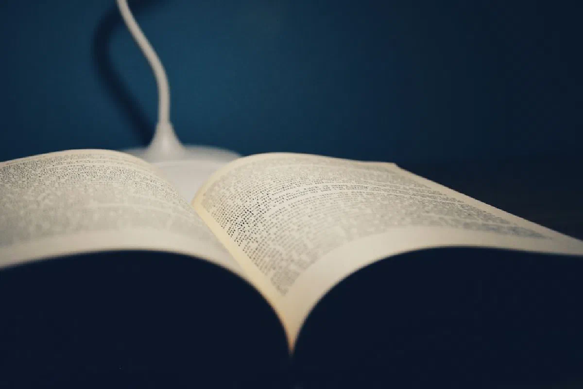 An open book on a table under the soft glow of a desk lamp, creating a study atmosphere.