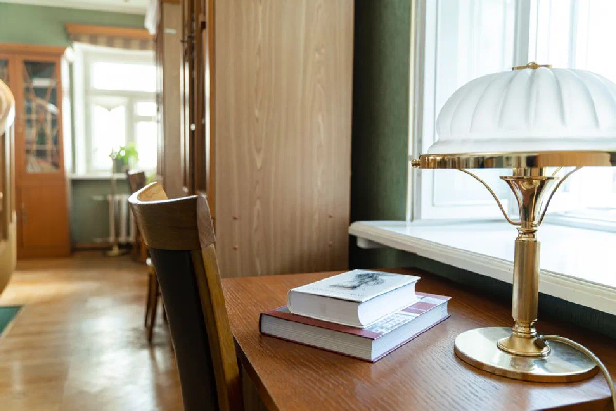 A cozy study area with books stacked beside a classic desk lamp in a softly lit room.