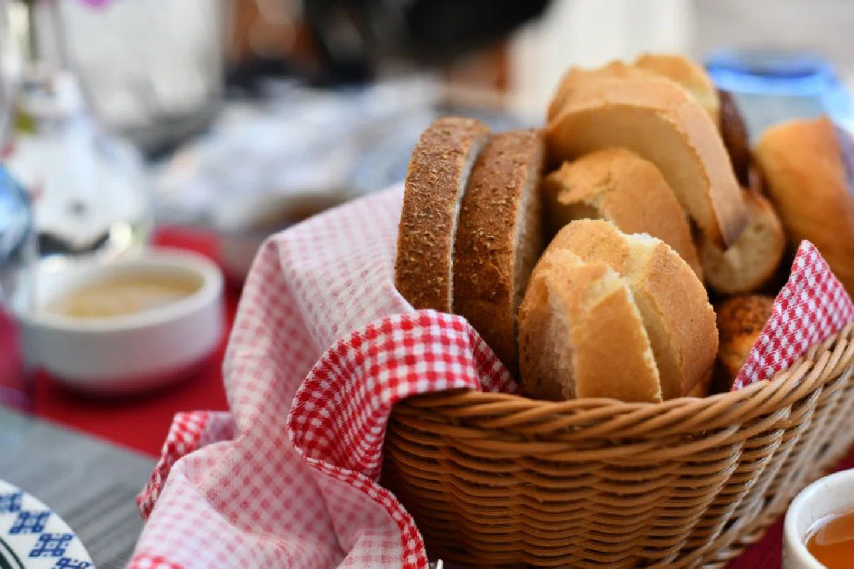 Assorted bread rolls in a wicker basket with red gingham cloth, perfect for breakfast.