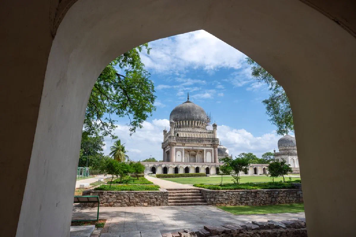 A stunning view of Qutb Shahi Tombs framed by an arch in Hyderabad, India, on a bright summer day.