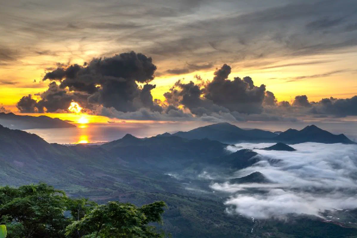 Stunning sunrise view with dramatic clouds and mist over a scenic mountain landscape.