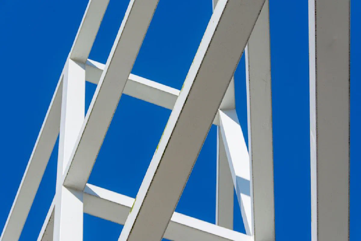 Low angle view of modern white beams forming abstract patterns against a bright blue sky.