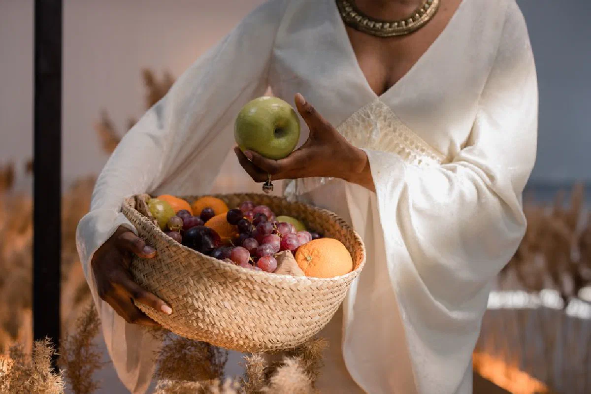 Elegant woman in white holding a woven basket of fresh fruits, showcasing modern lifestyle.