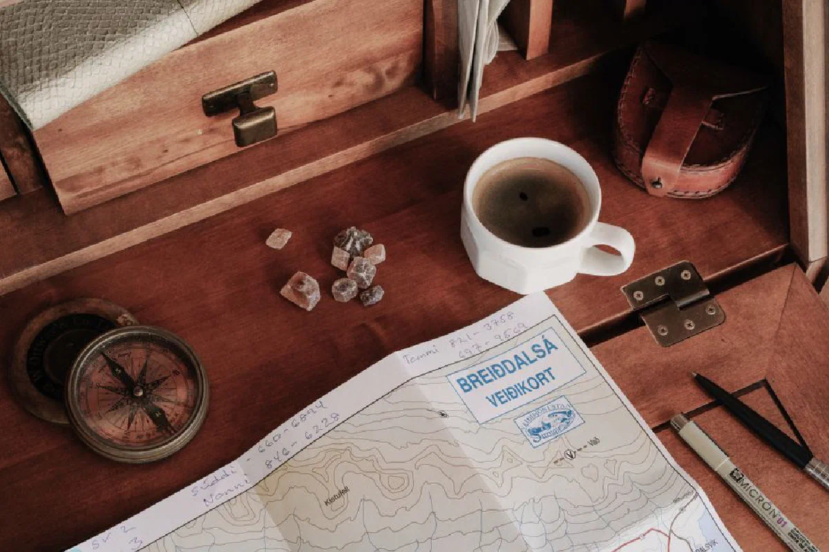 A top-down view of a rustic workspace featuring a map, compass, and a cup of coffee.