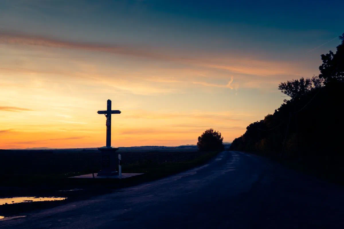Silhouette of a cross against a vibrant sunset sky in a peaceful rural setting, perfect for travel and nature themes.