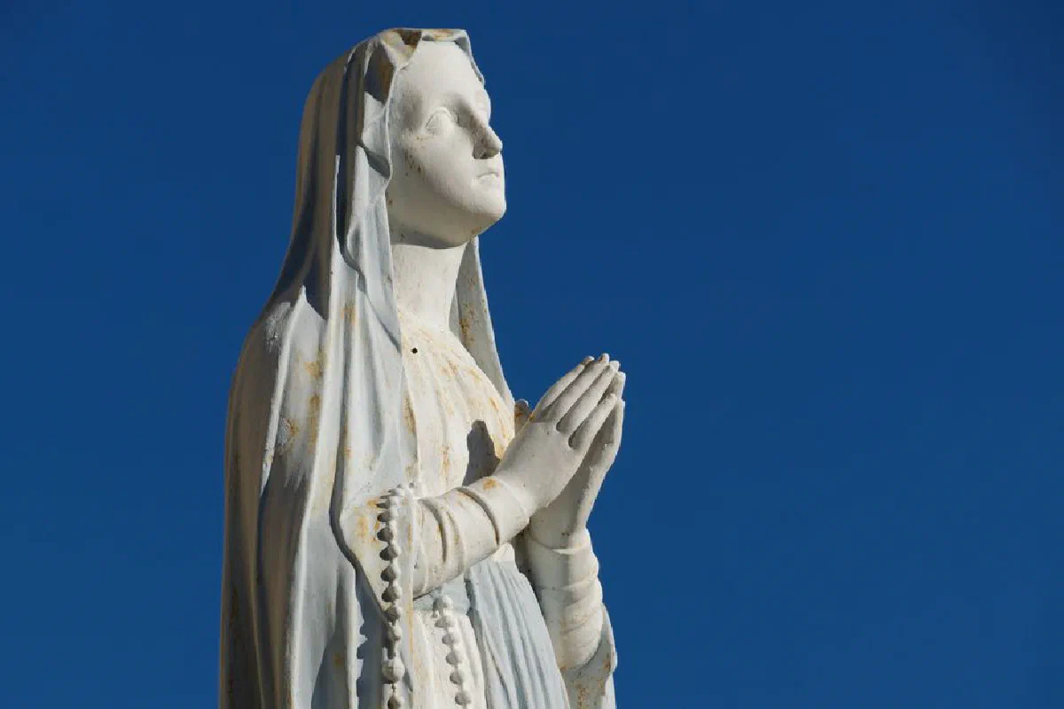 A serene statue of the Virgin Mary in prayer against a clear blue sky, symbolizing faith.
