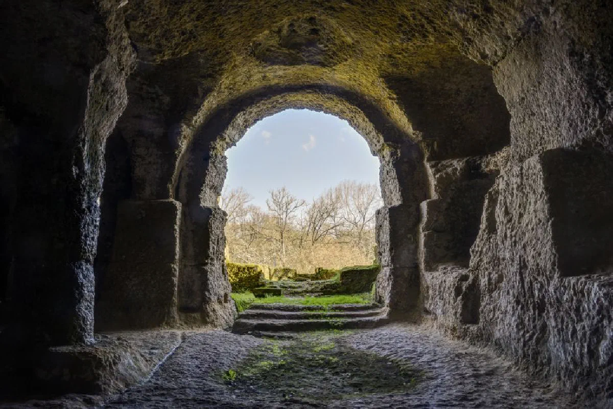 Stone cave entrance with natural light and surrounding trees in Gurat, France.