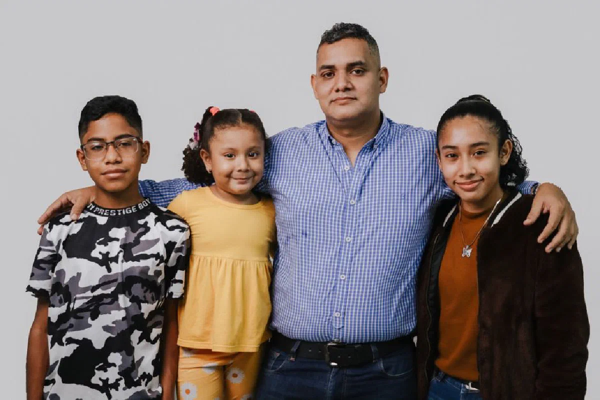 Portrait of a smiling father with his three children against a neutral background.
