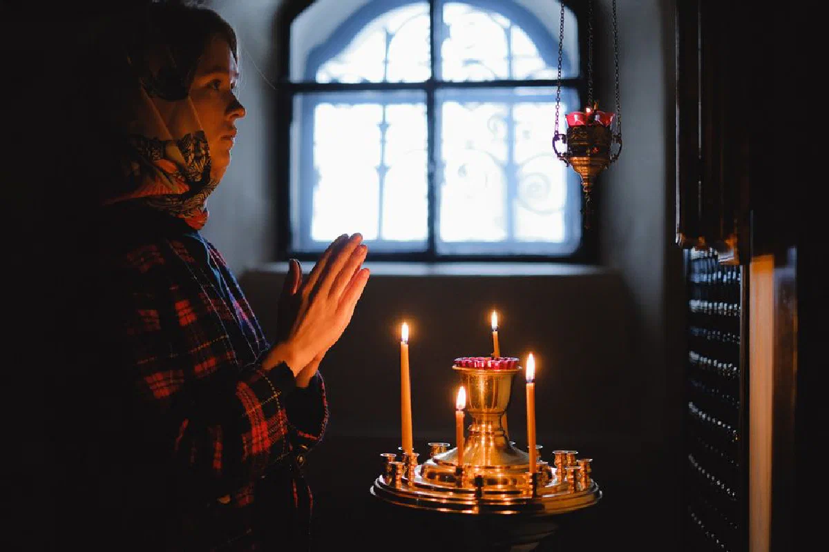 A woman in prayer by candlelight inside a church, conveying peace and contemplation.