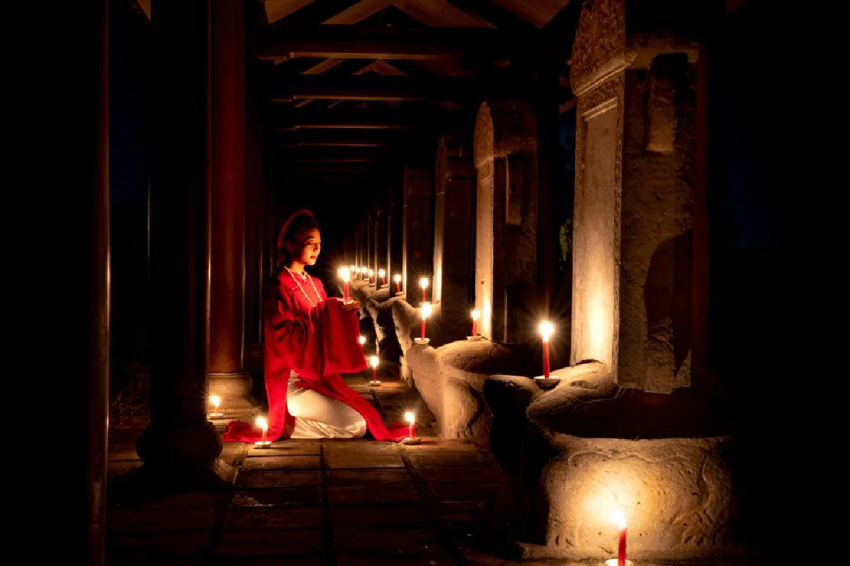Asian woman praying by candlelight in a traditional temple setting, evoking serenity and spirituality.