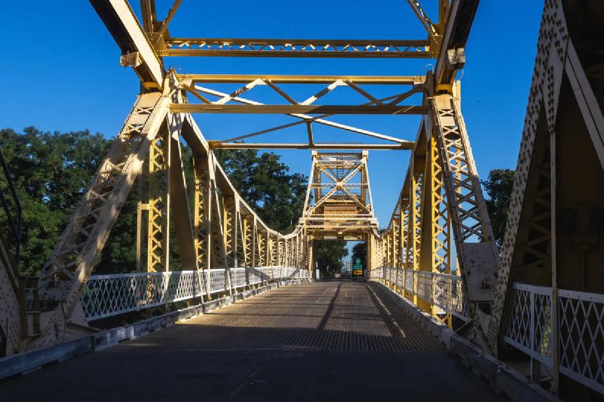 A historic steel truss bridge with intricate design under a clear blue sky, showing strong architectural details.
