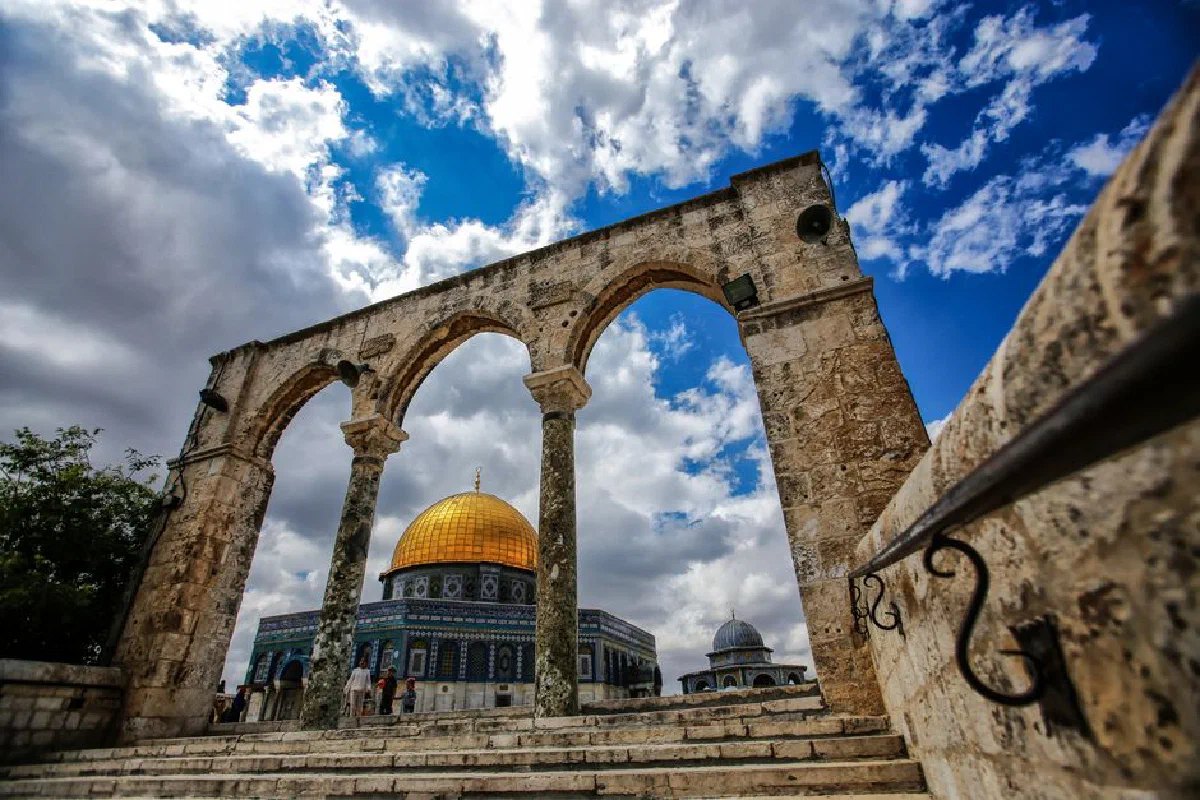 Stunning view of the Dome of the Rock in Jerusalem framed by ancient arches under a bright blue sky.