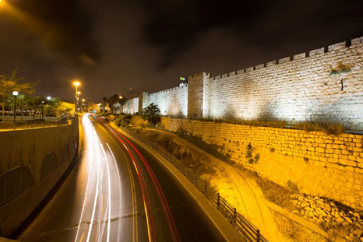 Nighttime photography of a historic stone wall with light trails from passing cars.