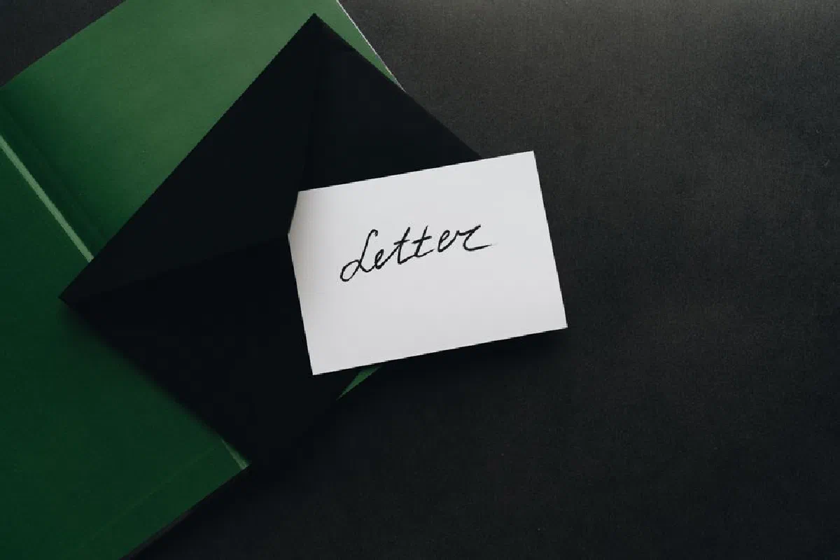 A flatlay showcasing a black envelope with a calligraphy letter, offering ample copyspace on a dark background.