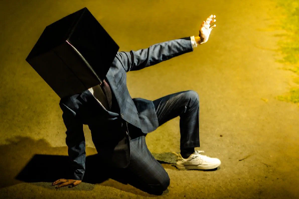 Artistic image of a man in a suit with a box on his head, outdoors at night.