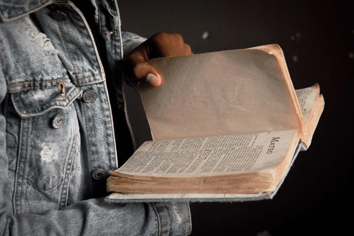 Person in denim jacket holding an open Bible, focusing on faith and spirituality.