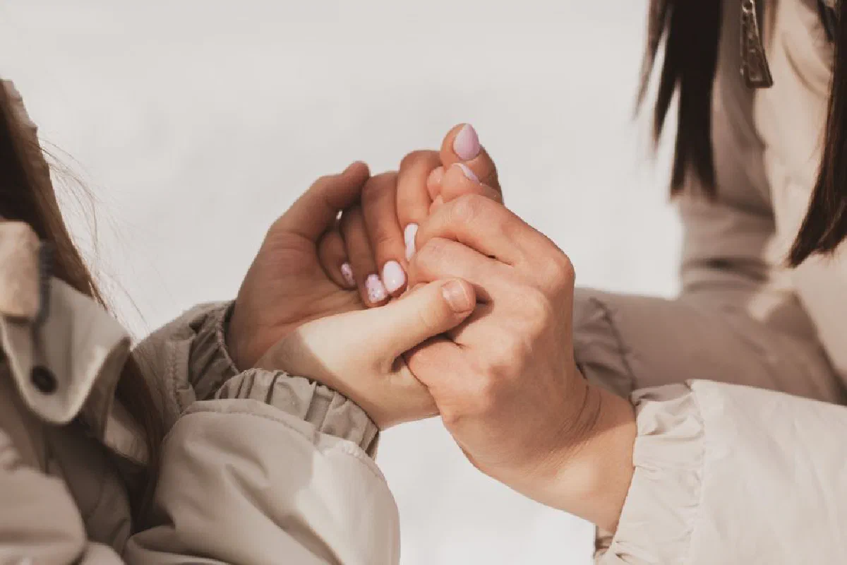 Close-up of two people holding hands warmly outdoors in winter.