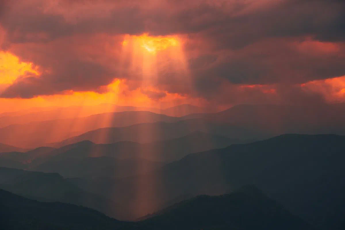 Stunning sun rays breaking through clouds over serene mountain ranges at sunset.
