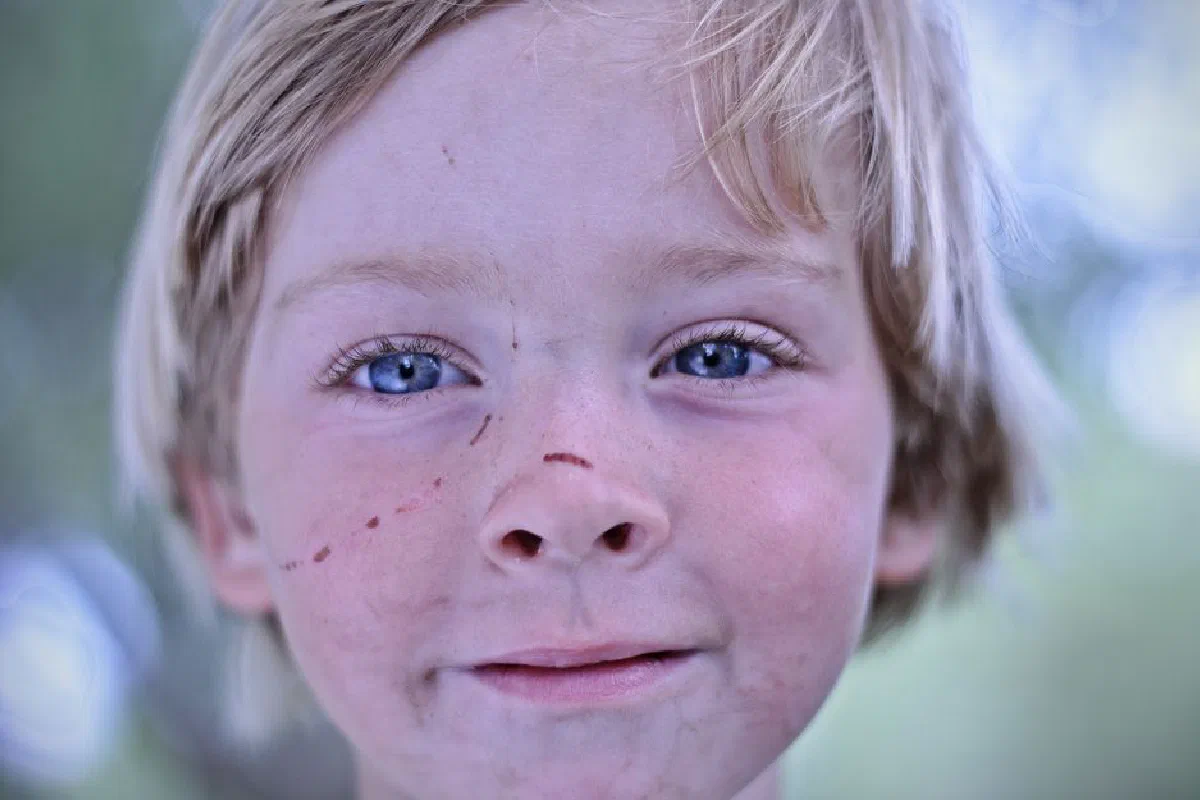 A cheerful child with freckles and blond hair enjoying a moment outdoors, smiling warmly.