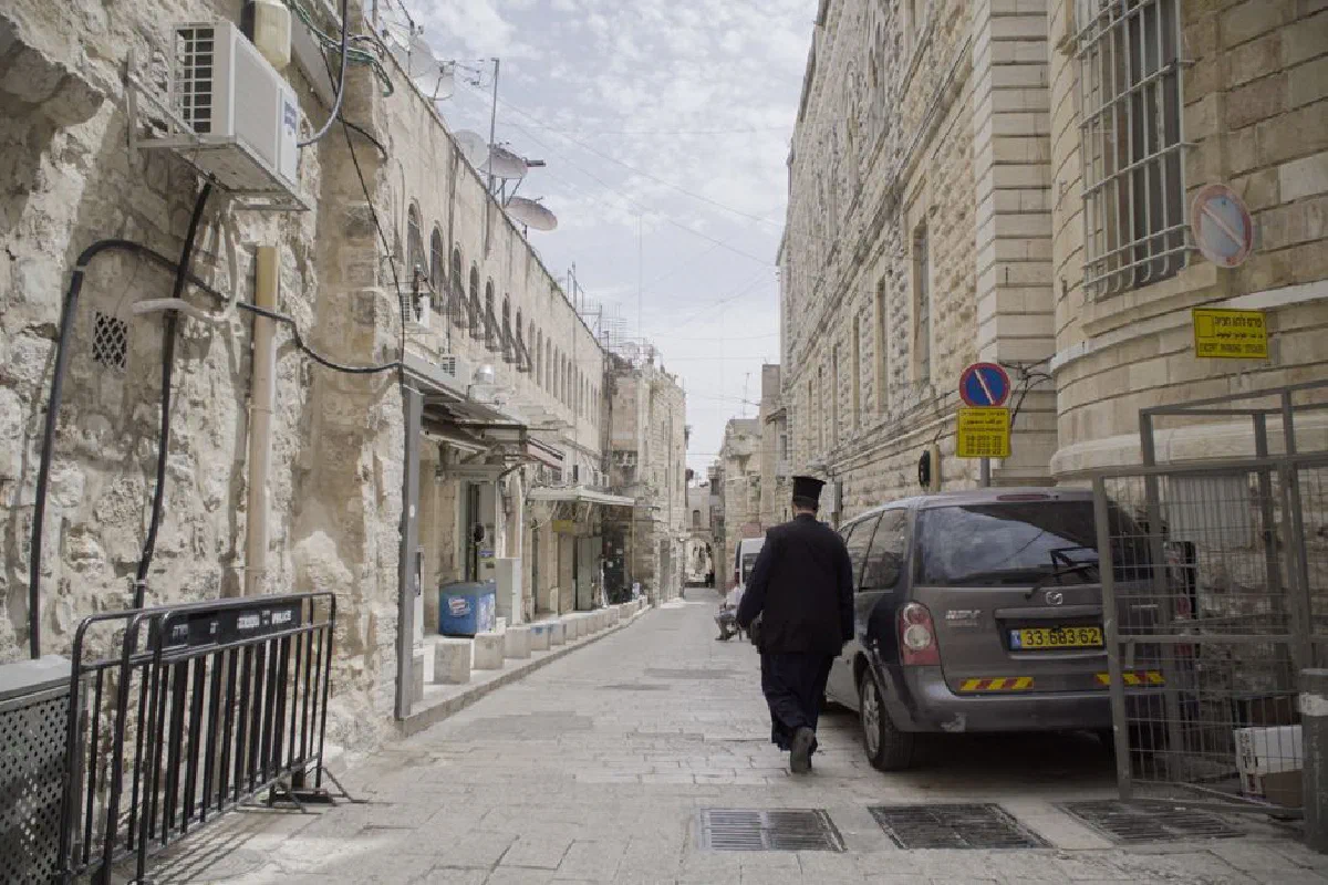 A man walks down a cobblestone street in a historic old city with stone buildings and narrow passageways.