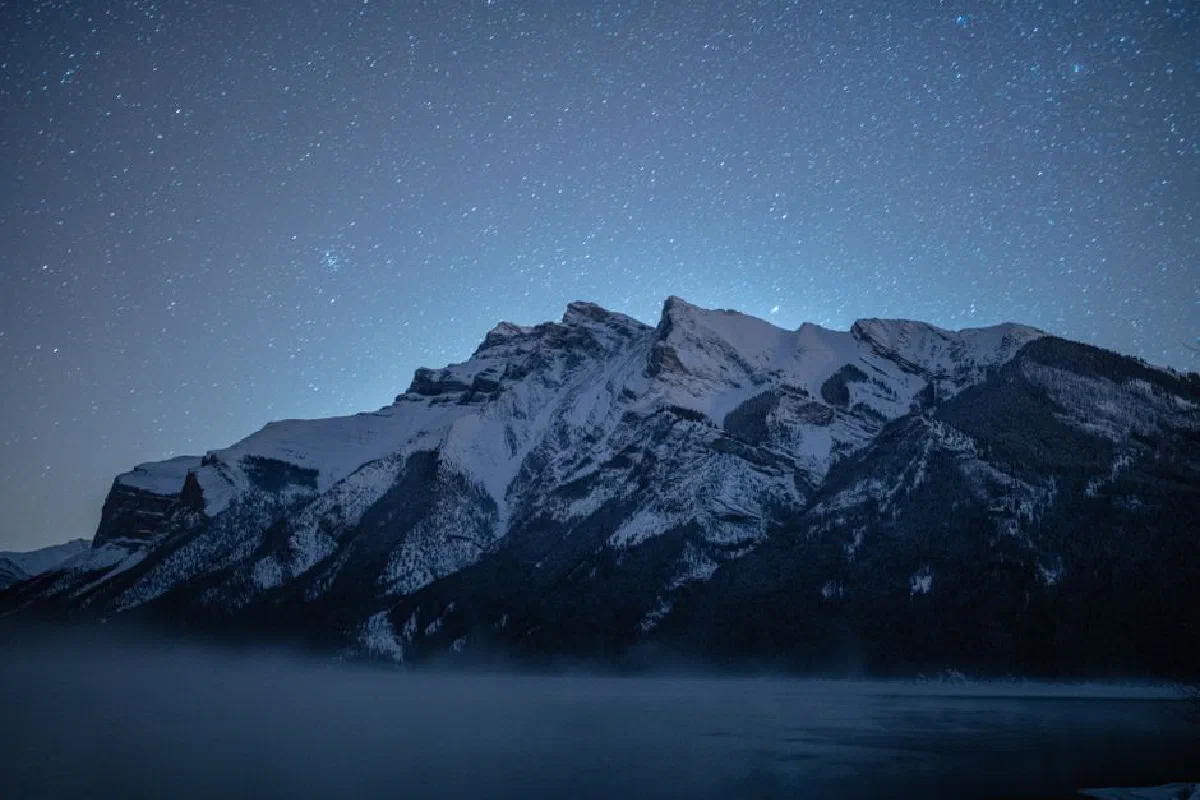 Stunning view of a snow-covered mountain peak in Canada under a clear starry night sky.