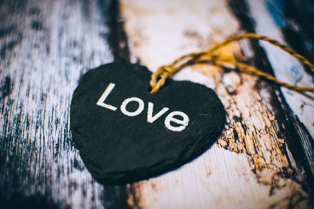 Close-up of a heart-shaped slate inscribed with 'Love' on a rustic wooden background, ideal for Valentine's themes.