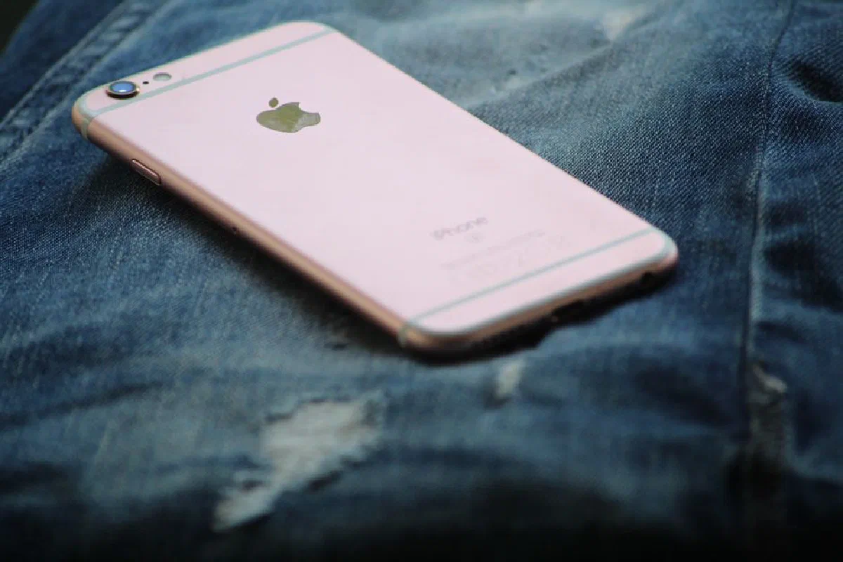 Pink smartphone placed on ripped denim jeans. Technology meets fashion in a close-up shot.