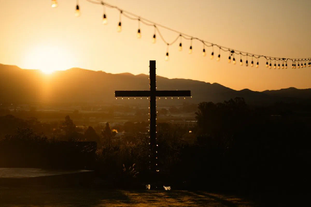 Silhouette of a cross with string lights at sunset, creating a serene ambiance.